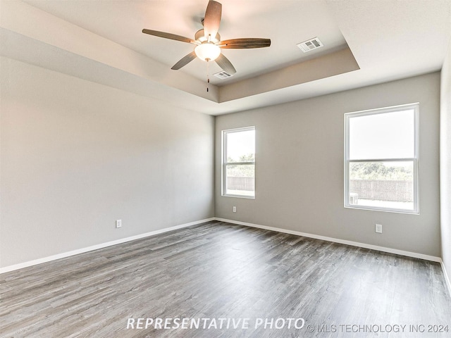 unfurnished room with ceiling fan, a tray ceiling, and dark hardwood / wood-style flooring