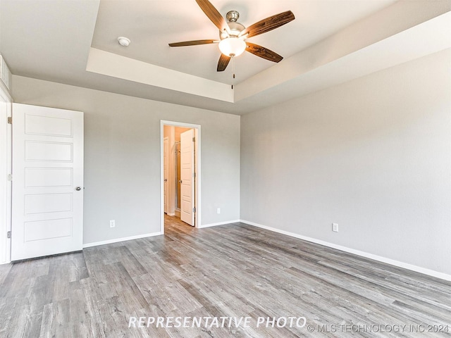 unfurnished bedroom featuring light wood-type flooring, a raised ceiling, and ceiling fan