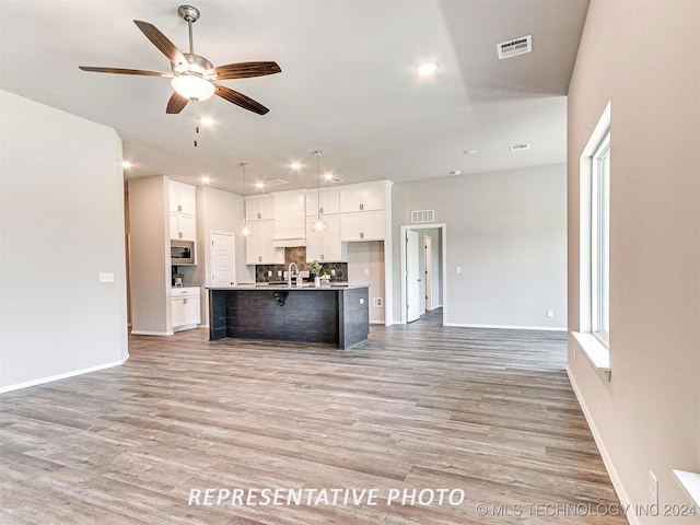 kitchen with a center island with sink, light hardwood / wood-style floors, hanging light fixtures, white cabinetry, and ceiling fan