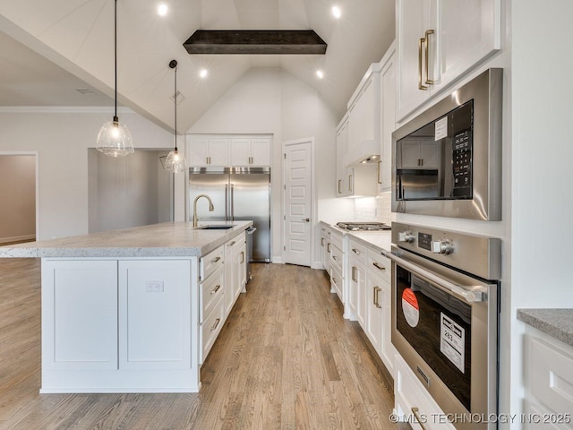 kitchen featuring pendant lighting, built in appliances, white cabinets, a center island with sink, and beamed ceiling