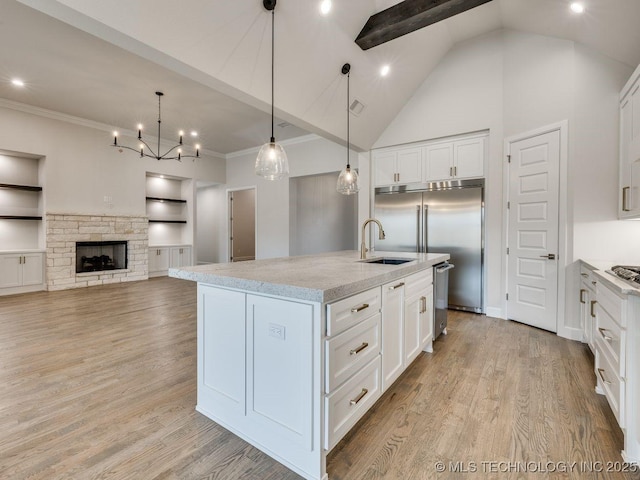 kitchen featuring a kitchen island with sink, sink, built in shelves, and white cabinets