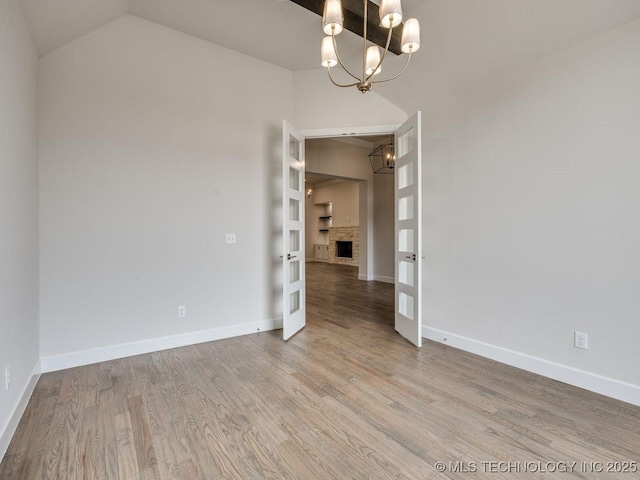 unfurnished room featuring a stone fireplace, hardwood / wood-style floors, lofted ceiling, an inviting chandelier, and french doors