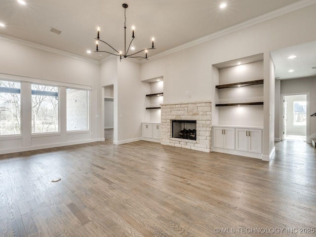 unfurnished living room with crown molding, a notable chandelier, a fireplace, built in shelves, and light wood-type flooring