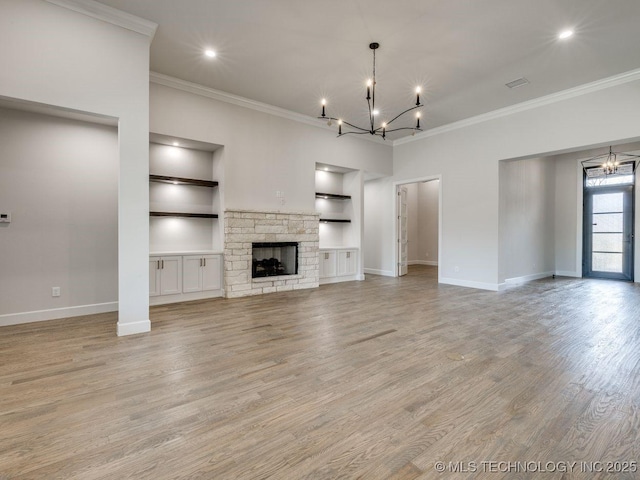 unfurnished living room with a fireplace, a chandelier, ornamental molding, built in shelves, and light hardwood / wood-style flooring