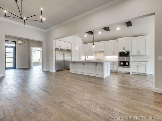 kitchen with white cabinets, decorative backsplash, a kitchen island with sink, built in appliances, and an inviting chandelier