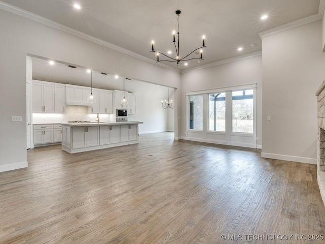 unfurnished living room featuring an inviting chandelier, sink, and light hardwood / wood-style floors