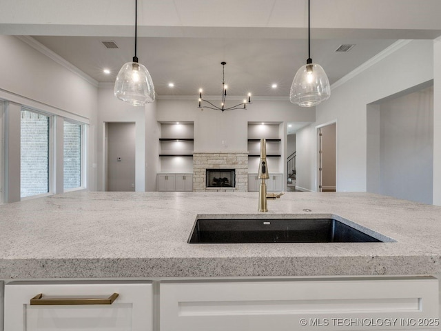 kitchen featuring pendant lighting, white cabinetry, a stone fireplace, and light stone countertops