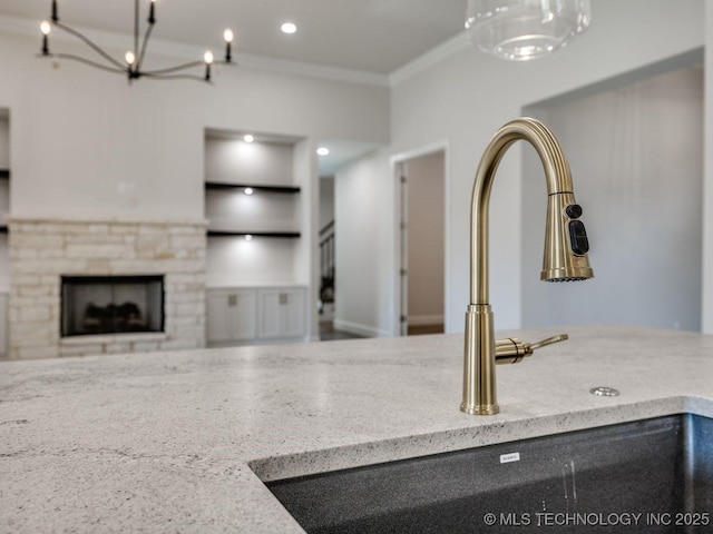 kitchen with built in shelves, a stone fireplace, sink, crown molding, and light stone countertops