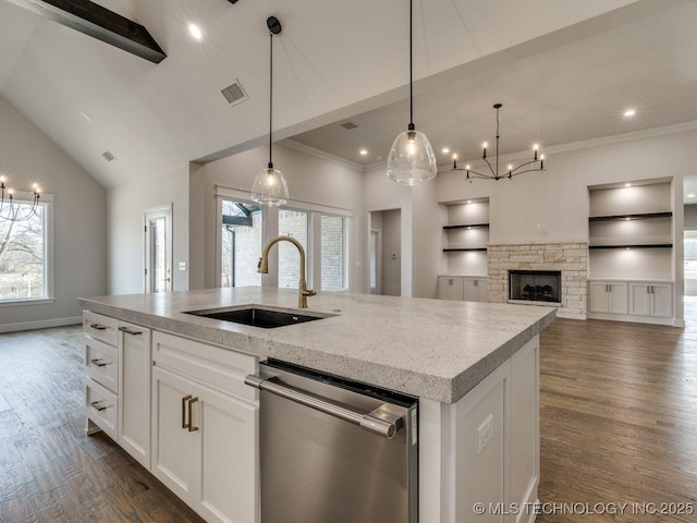 kitchen featuring built in shelves, sink, stainless steel dishwasher, a kitchen island with sink, and white cabinets