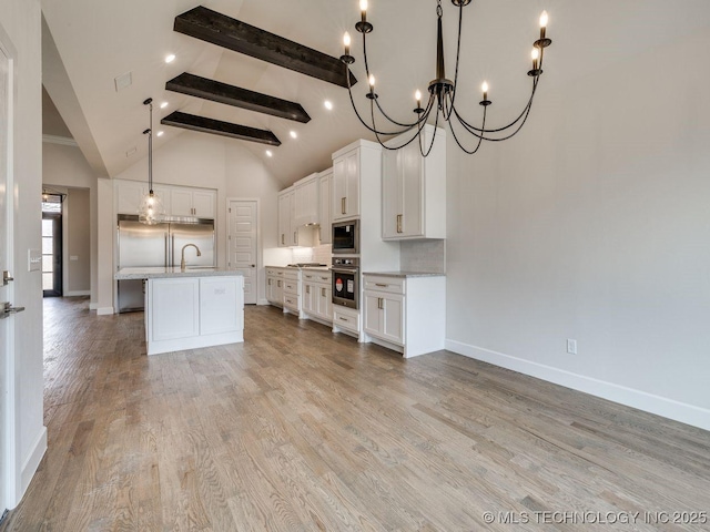 kitchen with tasteful backsplash, built in appliances, beam ceiling, a kitchen island with sink, and white cabinets