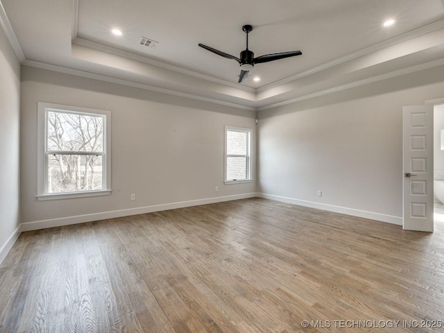 empty room featuring crown molding, ceiling fan, a tray ceiling, and light wood-type flooring