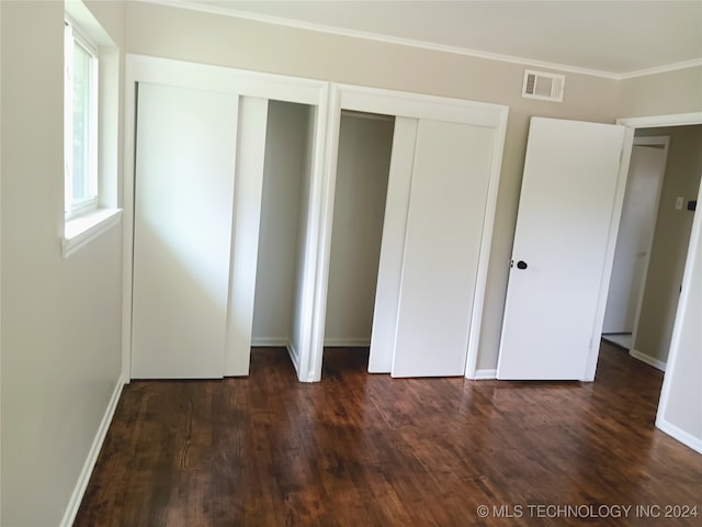 unfurnished bedroom with crown molding, dark wood-type flooring, and multiple closets