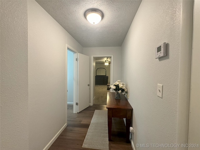 hall with a textured ceiling and dark wood-type flooring