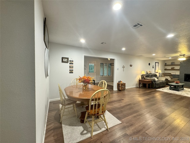 dining area featuring dark hardwood / wood-style flooring, ceiling fan, and a brick fireplace