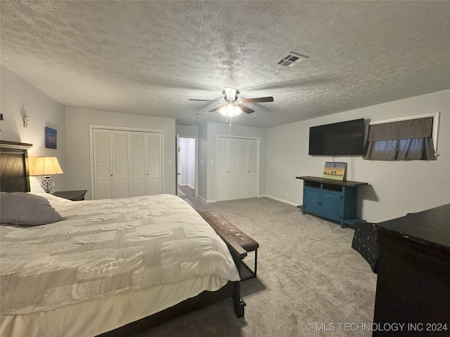 bedroom with two closets, ceiling fan, carpet floors, and a textured ceiling