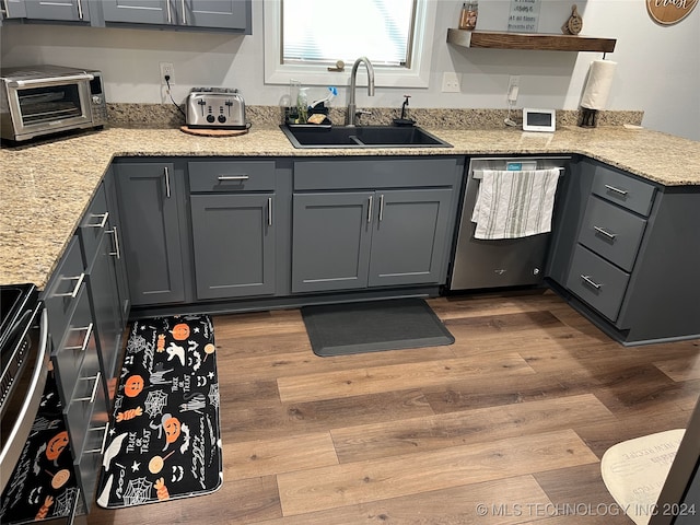 kitchen with appliances with stainless steel finishes, light stone countertops, gray cabinets, light wood-type flooring, and sink