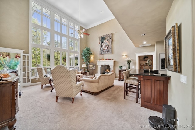 living room with ceiling fan, light carpet, ornamental molding, and a high ceiling