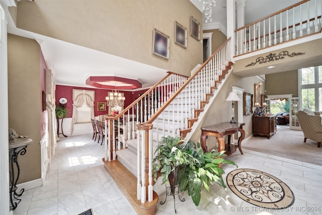 staircase featuring ornamental molding, a high ceiling, a notable chandelier, and carpet