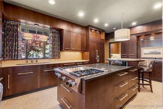 kitchen with stainless steel gas cooktop, a center island, a kitchen breakfast bar, hanging light fixtures, and dark stone counters