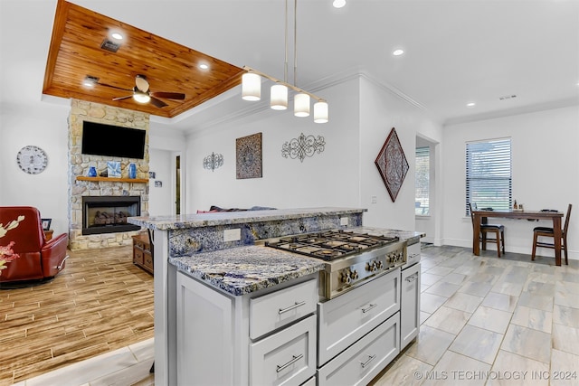 kitchen with ornamental molding, stainless steel gas cooktop, white cabinets, a stone fireplace, and dark stone counters