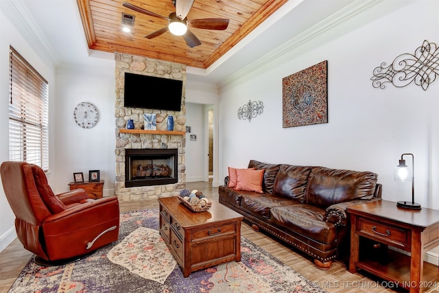 living room with a stone fireplace, a tray ceiling, ornamental molding, light hardwood / wood-style floors, and wood ceiling