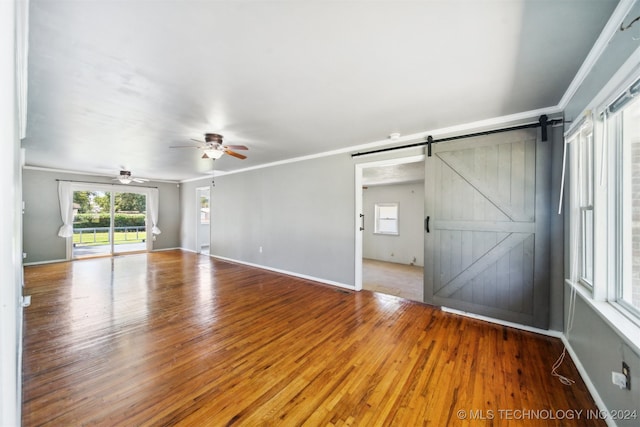 unfurnished room featuring crown molding, hardwood / wood-style floors, ceiling fan, and a barn door