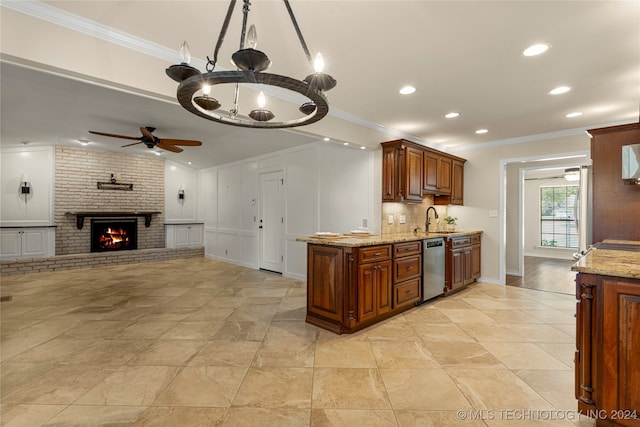 kitchen featuring ceiling fan with notable chandelier, ornamental molding, a brick fireplace, light stone counters, and stainless steel dishwasher