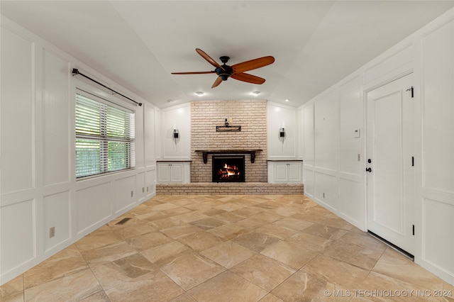 unfurnished living room featuring lofted ceiling, ceiling fan, brick wall, and a brick fireplace