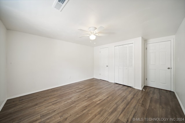 unfurnished bedroom with ceiling fan, multiple closets, and dark hardwood / wood-style flooring