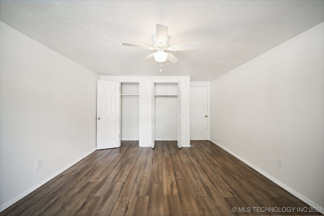 unfurnished bedroom with two closets, dark hardwood / wood-style floors, and ceiling fan