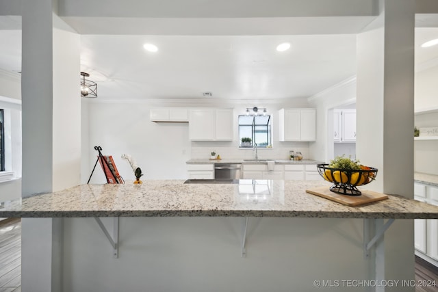 kitchen featuring white cabinets, ornamental molding, wood-type flooring, a kitchen breakfast bar, and light stone countertops