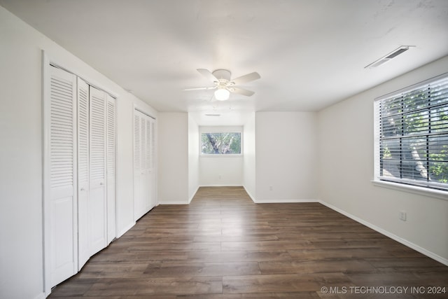 unfurnished bedroom with two closets, ceiling fan, and dark hardwood / wood-style flooring