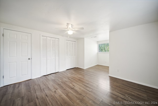 unfurnished bedroom featuring multiple closets, ceiling fan, and hardwood / wood-style flooring