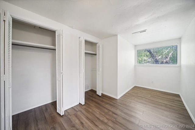 unfurnished bedroom with dark hardwood / wood-style flooring and multiple closets