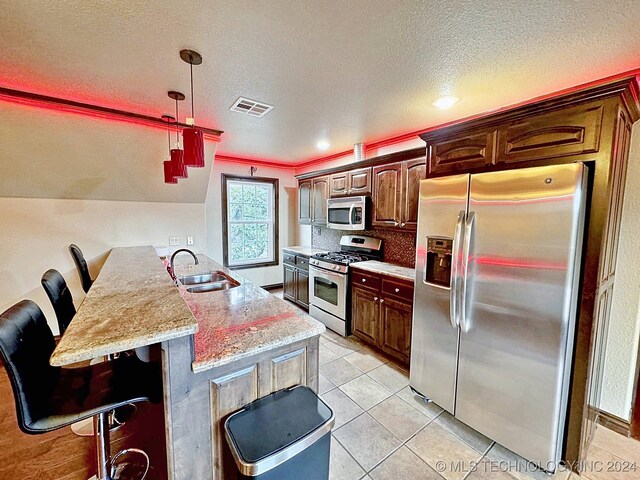 kitchen featuring stone countertops, a textured ceiling, a kitchen bar, sink, and appliances with stainless steel finishes