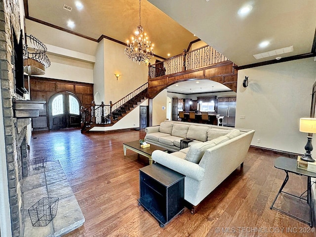 living room with a fireplace, a high ceiling, a notable chandelier, ornamental molding, and dark hardwood / wood-style flooring