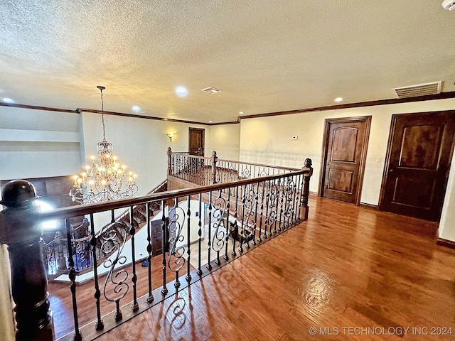 corridor featuring crown molding, hardwood / wood-style flooring, a textured ceiling, and a chandelier