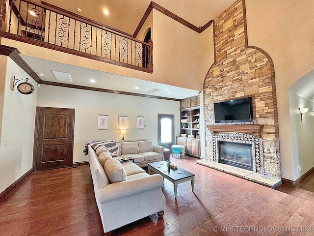 living room featuring built in features, dark wood-type flooring, a high ceiling, and a stone fireplace