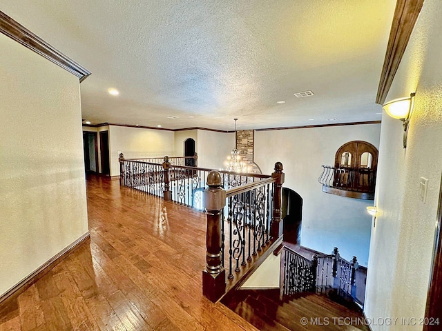 hallway with wood-type flooring, an inviting chandelier, crown molding, and a textured ceiling