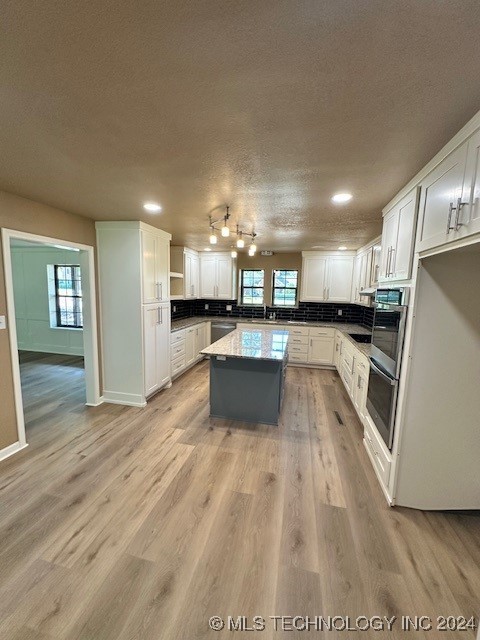 kitchen with plenty of natural light, a center island, white cabinets, and light hardwood / wood-style floors