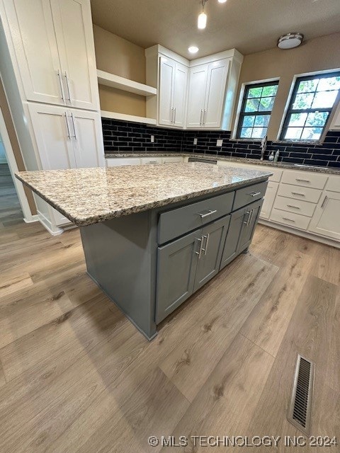 kitchen featuring white cabinets, gray cabinetry, light wood-type flooring, light stone counters, and a kitchen island