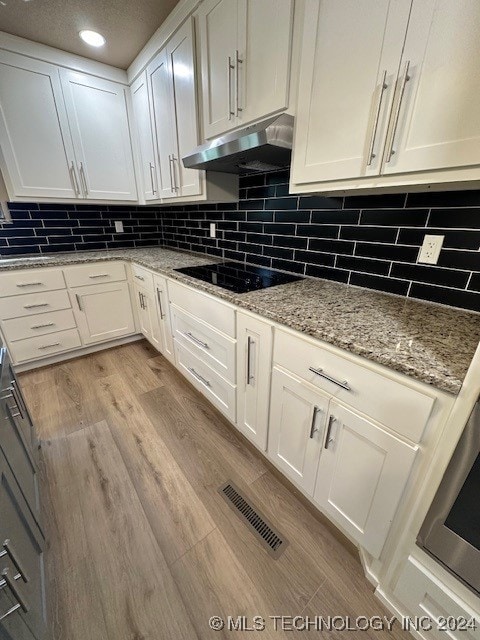 kitchen featuring backsplash, light wood-type flooring, light stone counters, white cabinetry, and black electric stovetop