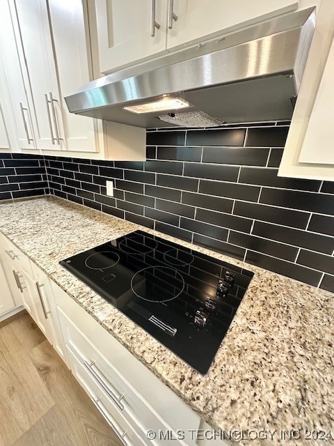 kitchen featuring light wood-type flooring, backsplash, light stone countertops, black electric cooktop, and white cabinets