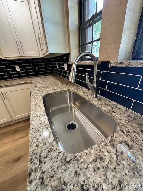 room details with hardwood / wood-style floors, light stone counters, white cabinetry, and sink