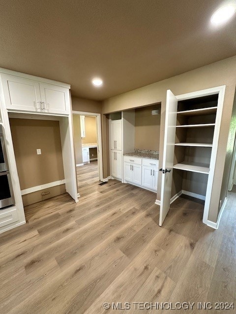 kitchen featuring a textured ceiling, oven, light hardwood / wood-style floors, white cabinetry, and light stone counters