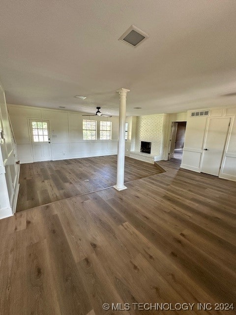 unfurnished living room with a wealth of natural light, a large fireplace, ceiling fan, and dark wood-type flooring