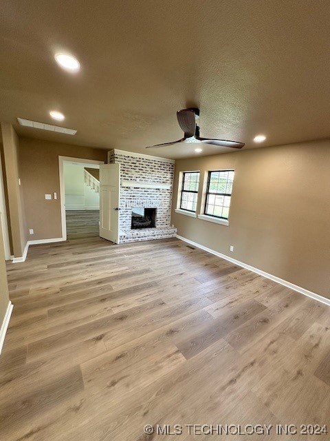 unfurnished living room featuring a textured ceiling, light hardwood / wood-style flooring, ceiling fan, and a brick fireplace