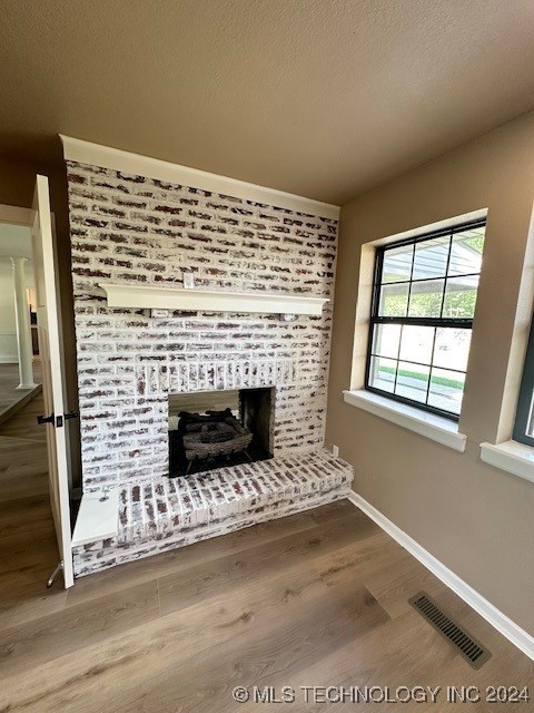 unfurnished living room featuring hardwood / wood-style floors, a textured ceiling, and a brick fireplace