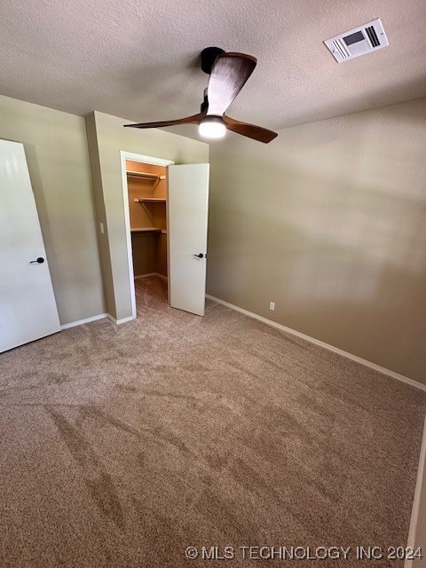 unfurnished bedroom featuring a textured ceiling, a spacious closet, a closet, light carpet, and ceiling fan