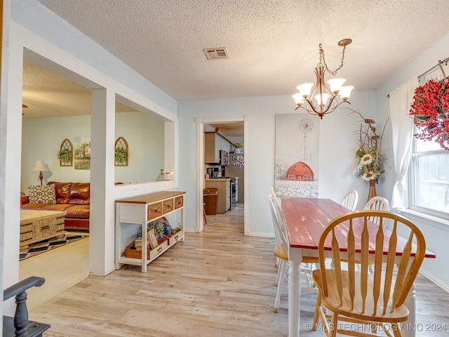 dining area with a textured ceiling, a notable chandelier, and light hardwood / wood-style floors